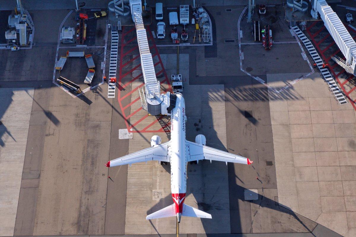 Aircraft docked at airport gate with jet bridge and ground service vehicles, showcasing operational facilities available to airline partners at QAL.