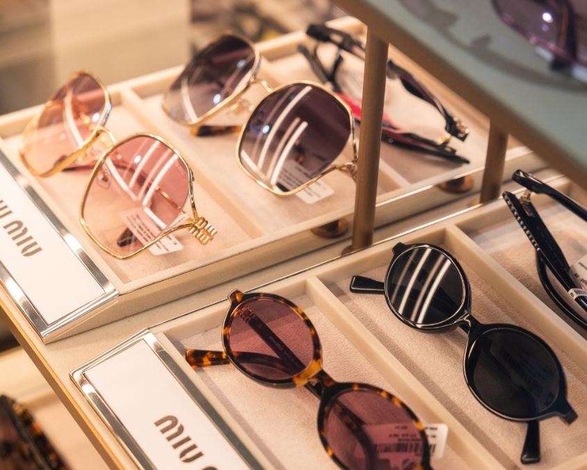 A display of designer Miu Miu sunglasses in various styles and colours, including pink, tortoiseshell, and black frames, neatly arranged in a retail case.