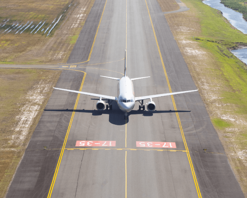 A commercial aircraft is positioned on the taxiway at Gold Coast Airport, viewed from above. The runway markings and surrounding grassy areas are clearly visible.