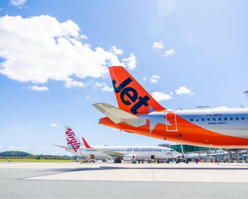 Three aircraft parked at the Gold Coast Airport terminal including Jetstar Airbus A320 VH-VFU, Virgin Australia aircraft, and a smaller regional plane.