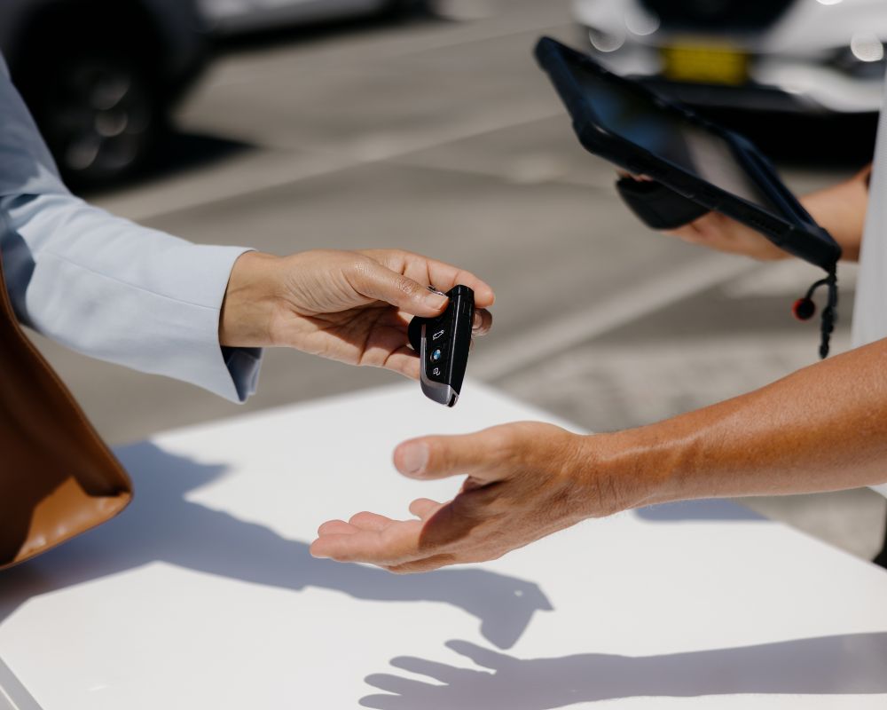 A close-up of a person handing over car keys to a valet attendant at Gold Coast Airport, with a tablet in the background for check-in.